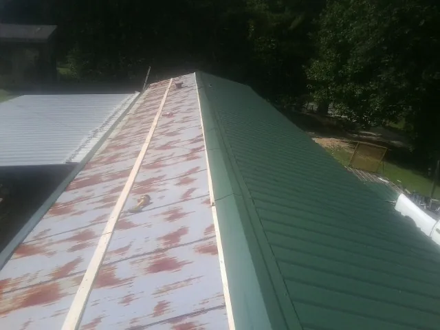 Old rusted panels beside newly installed green metal roofing — Wind Damage Roof Repair by Roofing Brothers in Boone